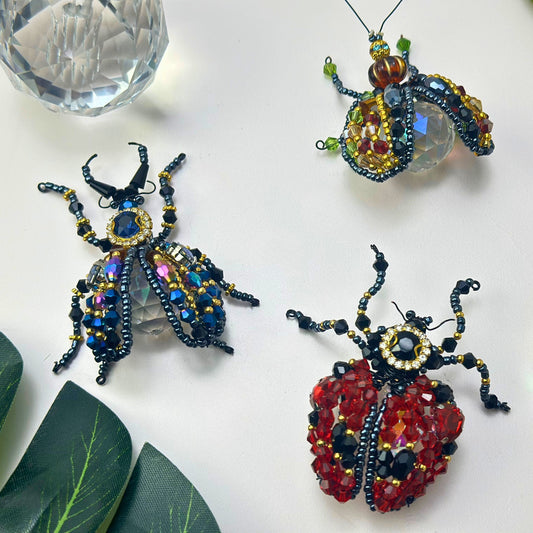 Colorful beaded beetle ornaments on a white surface with green leaves.