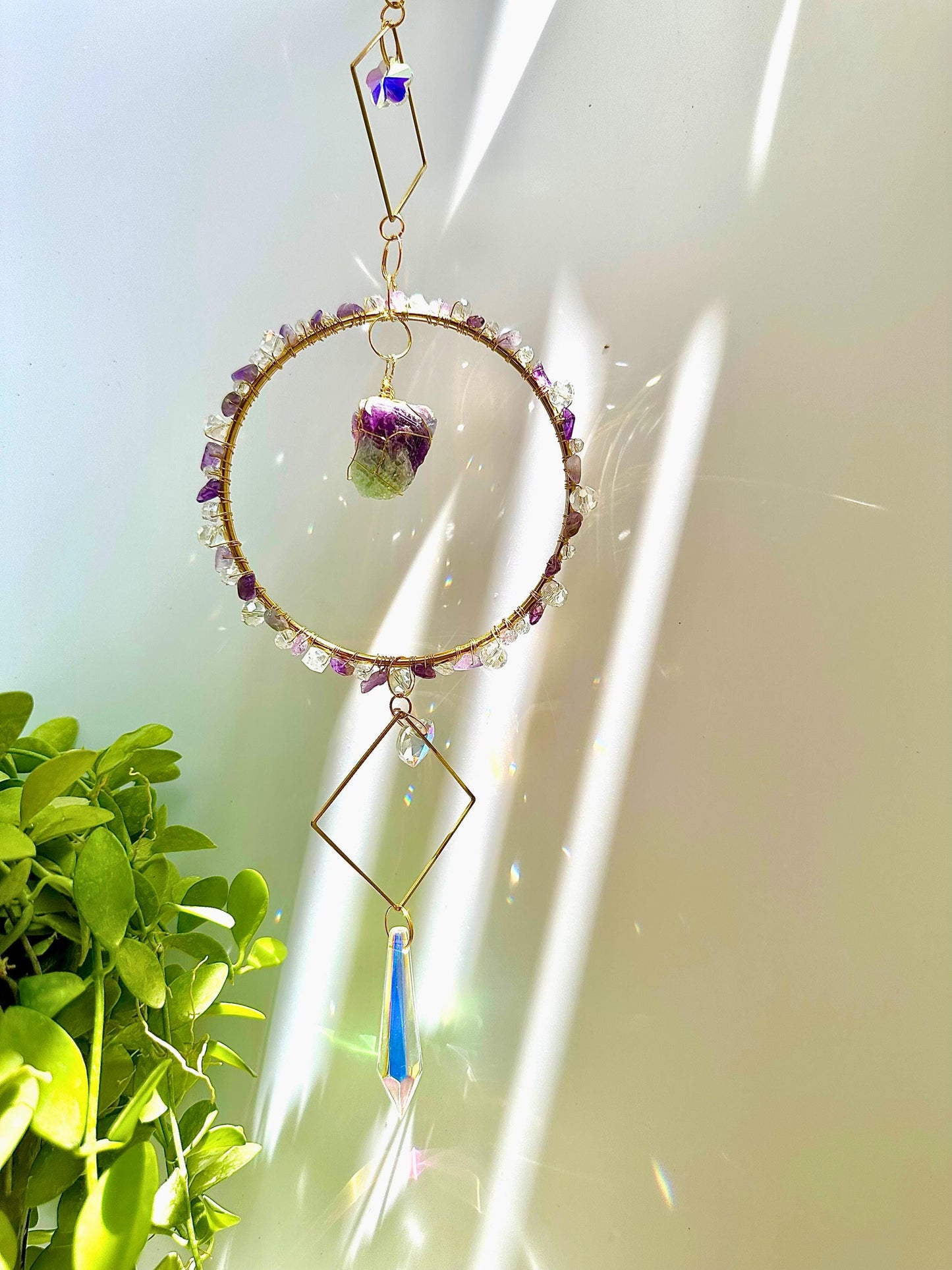 Radiant crystal and raw gemstone suncatcher with gold accents and pastel stones, hanging by a bright window with plant decor, capturing sparkly rainbow light reflections.