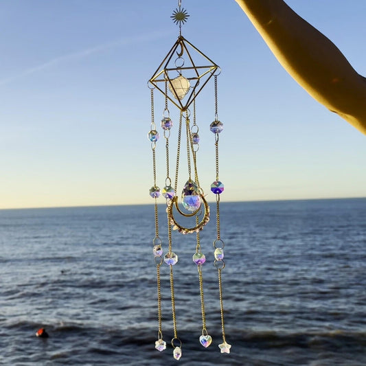 Close-up of a boho crystal suncatcher with rose quartz and faceted beads,
catching golden sunset light over the ocean horizon