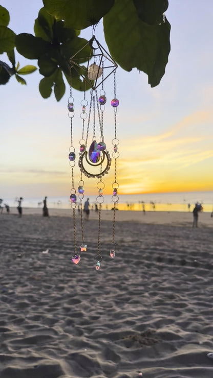 Mystical hanging sun catcher shown under a beach tree at twilight,
layered with star, heart and faceted beads reflecting soft pink hues.