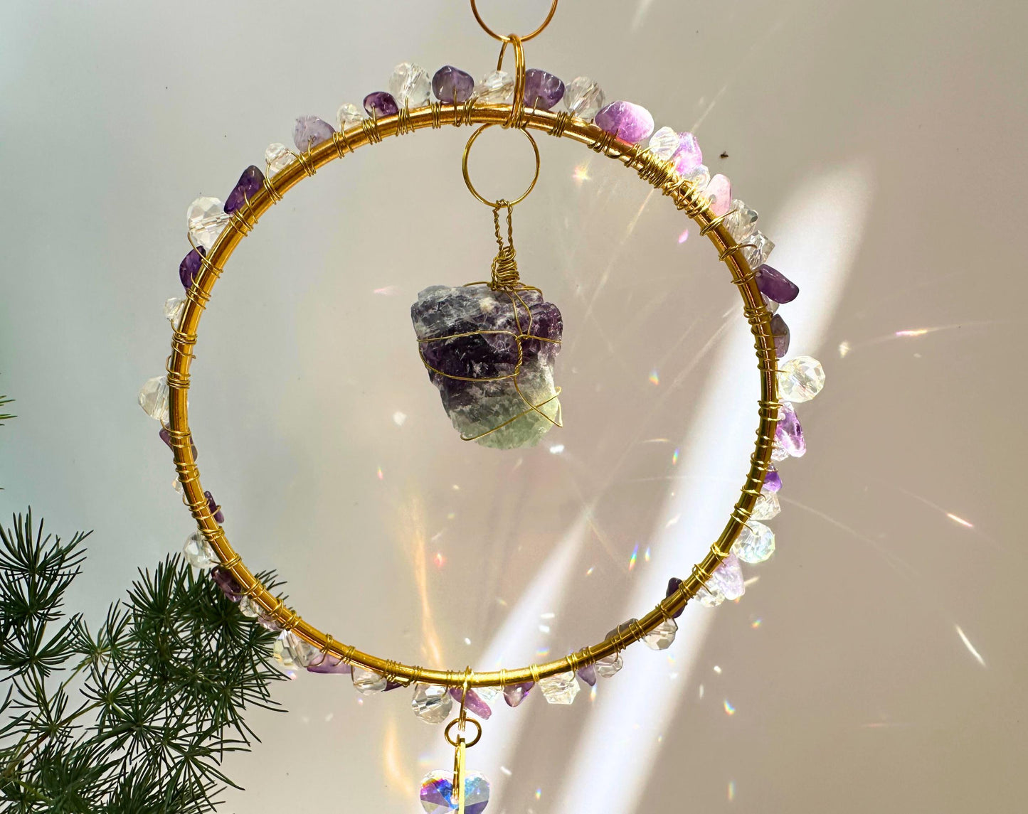 Macro photo of the central gemstone and bead details of a circular crystal suncatcher, glowing in sunlight, highlighting the intricate wrapping and light refraction.